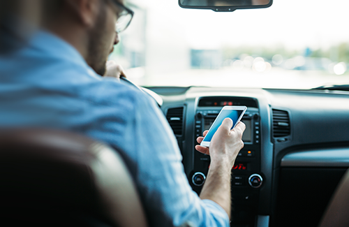 A man checks his cell phone while driving a car.