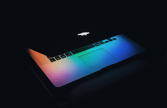 A laptop in the dark with a colorful glowing screen.