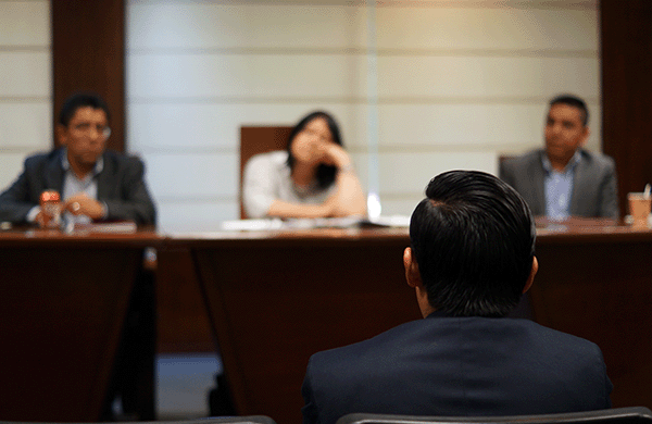 The back of a man's head as he faces a panel of three others in a professional environment.