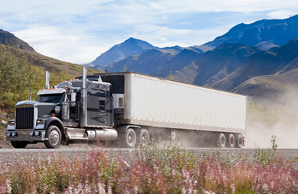 A black semi truck with a white trailer drives with mountains in the background.