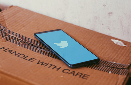 Cell Phone showing Twitter logo atop a box labeled "Handle with Care"