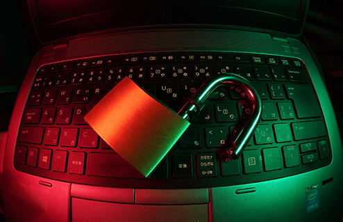 An open padlock atop a computer keyboard with glowing red and green light.