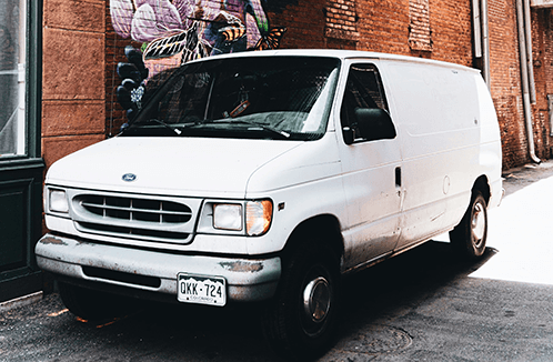 White Ford van parked in front of a brick wall.